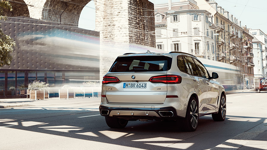 BMW X5 (G05) ketvirtoji karta, pastatų fone stovinčio automobilio trijų ketvirčių vaizdas iš galo BMW X serijos BMW X5 (G05) ketvirtoji karta, pastatų fone stovinčio automobilio trijų ketvirčių vaizdas iš galo