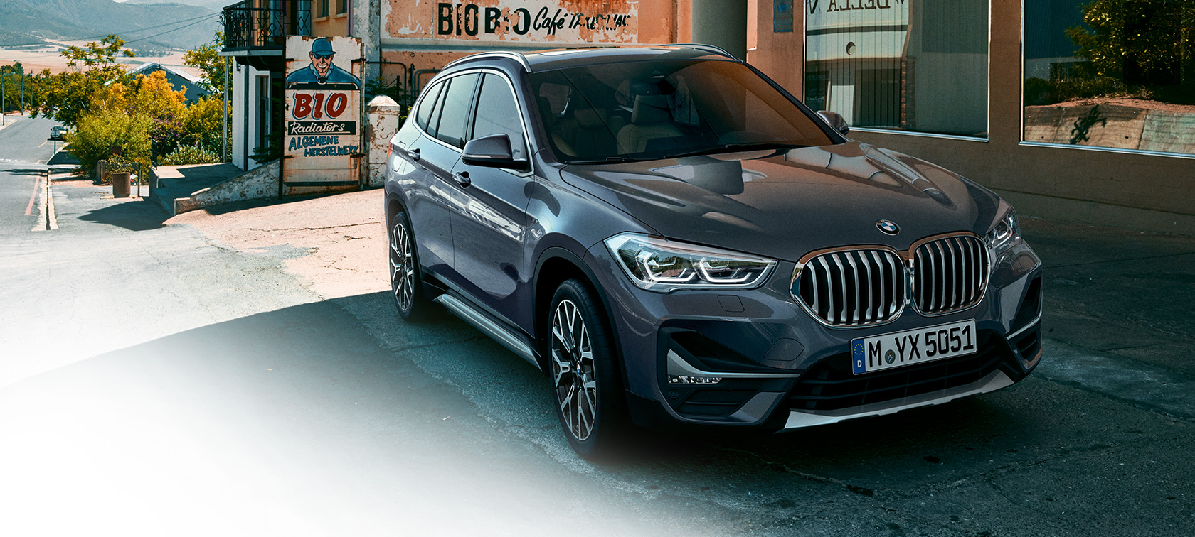 BMW X1, trijų ketvirčių vaizdas iš priekio. BMW X1, miesto fone stovinčio automobilio trijų ketvirčių vaizdas iš priekio.
