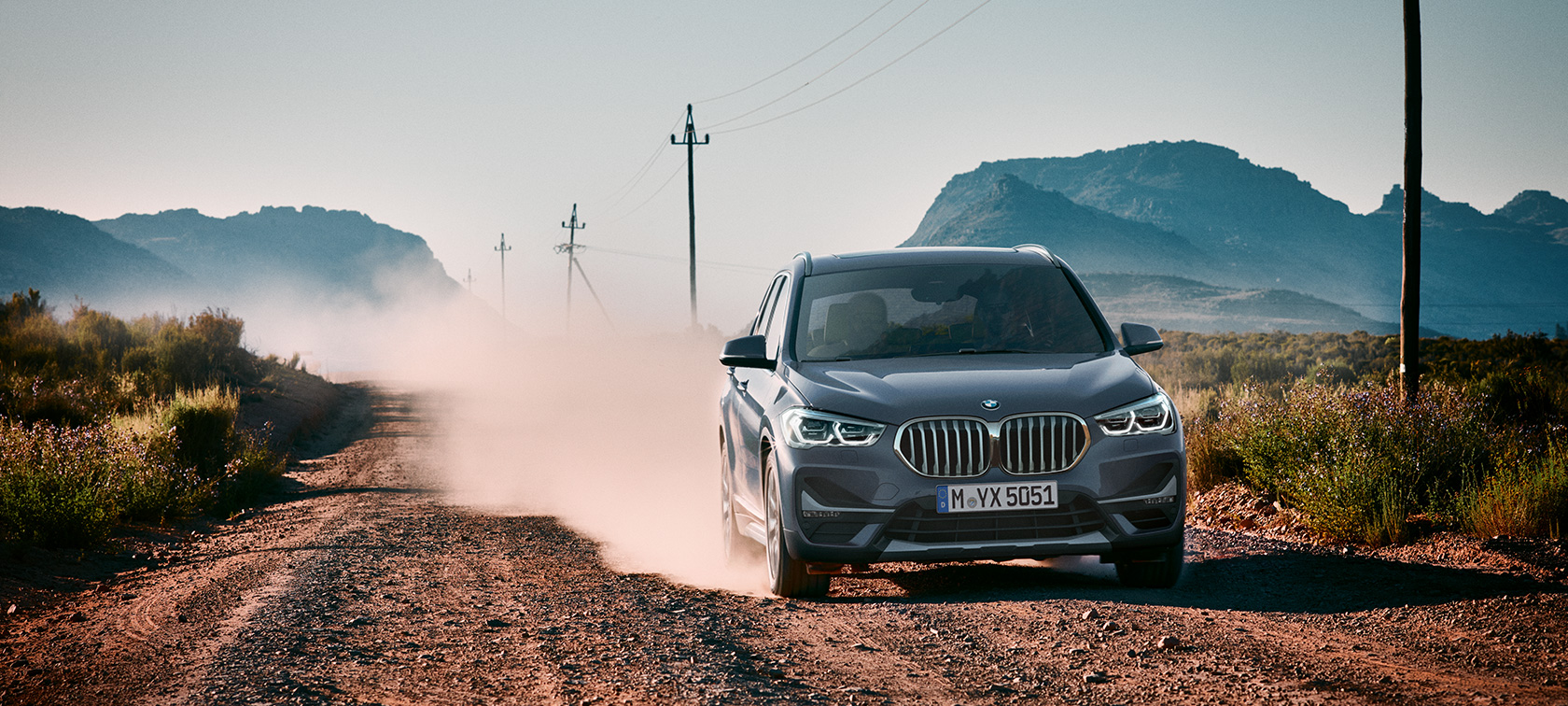 BMW X1, trijų ketvirčių vaizdas iš galo. BMW X1, važiuojančio kalnų fone automobilio trijų ketvirčių vaizdas iš galo.