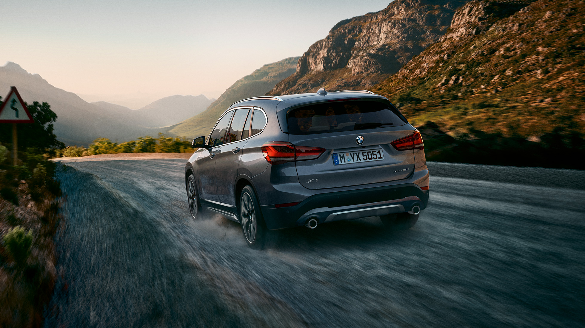BMW X1, trijų ketvirčių vaizdas iš galo. BMW X1, važiuojančio kalnų fone trijų ketvirčių vaizdas iš galo.