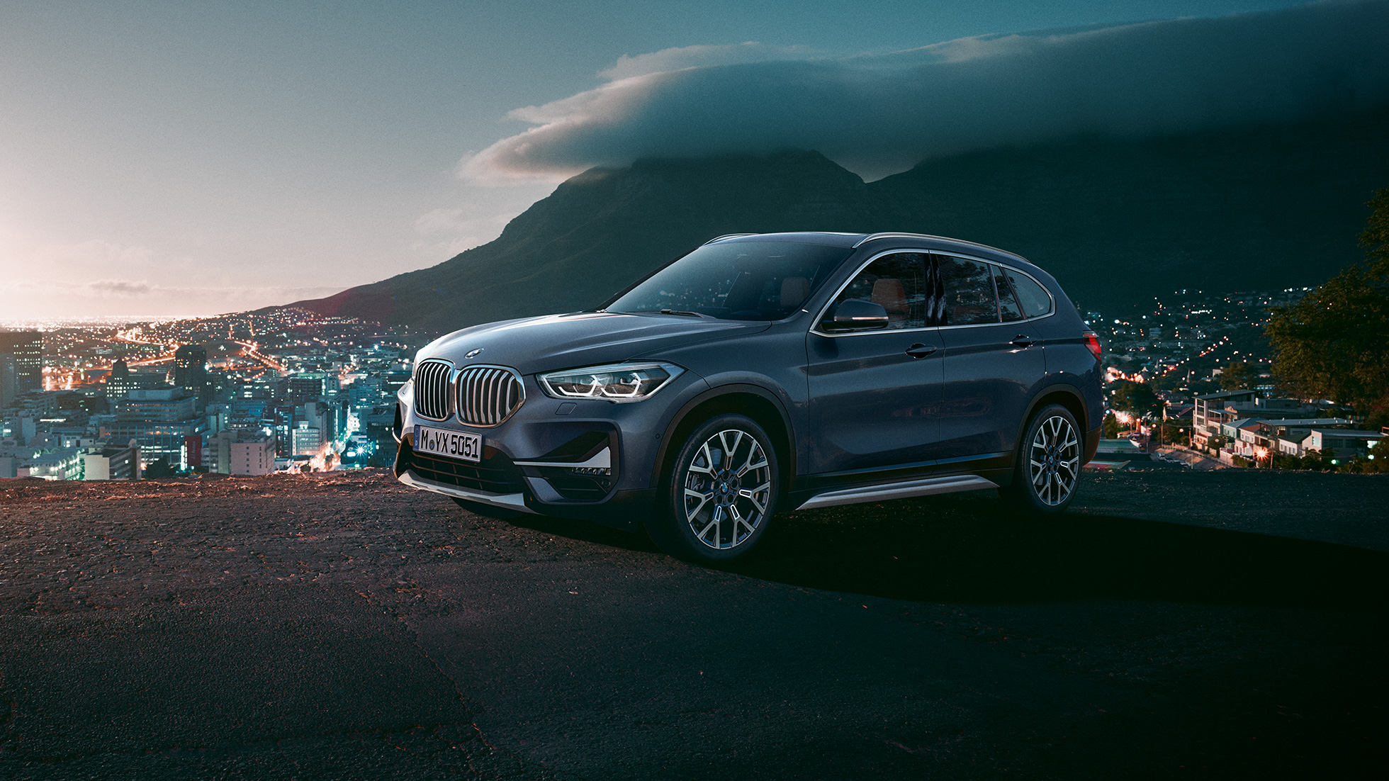 BMW X1, trijų ketvirčių vaizdas iš šono. BMW X1, miesto fone stovinčio automobilio trijų ketvirčių vaizdas iš šono.