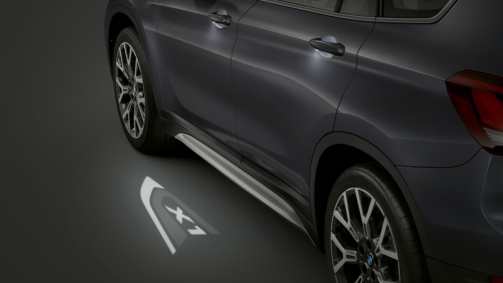 BMW X1, LED-projekcija „X1“. BMW X1, šoninis vaizdas su LED projekcija „X1“ stambiu planu.