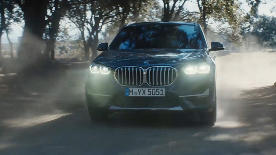 BMW X1 (F48) LCI trijų ketvirčių vaizdas iš priekio BMW X1 (F48) LCI, gamtos fone važiuojančio automobilio trijų ketvirčių vaizdas iš priekio