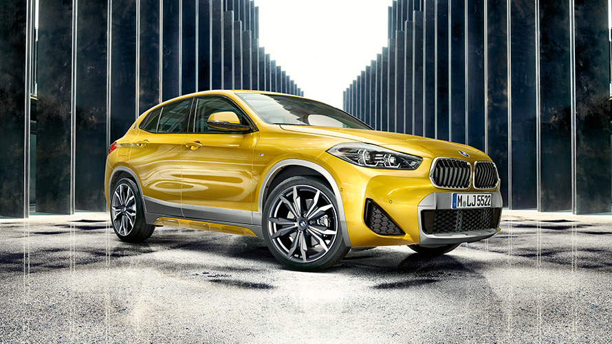 BMW X2 (F39) pilkos Brooklyn Grey spalvos, trijų ketvirčių vaizdas iš galo su atviromis durelėmis ir dviem žmonėmis BMW X2 (F39) pilkos Brooklyn Grey spalvos, trijų ketvirčių vaizdas iš galo su atviromis durelėmis ir dviem žmonėmis
