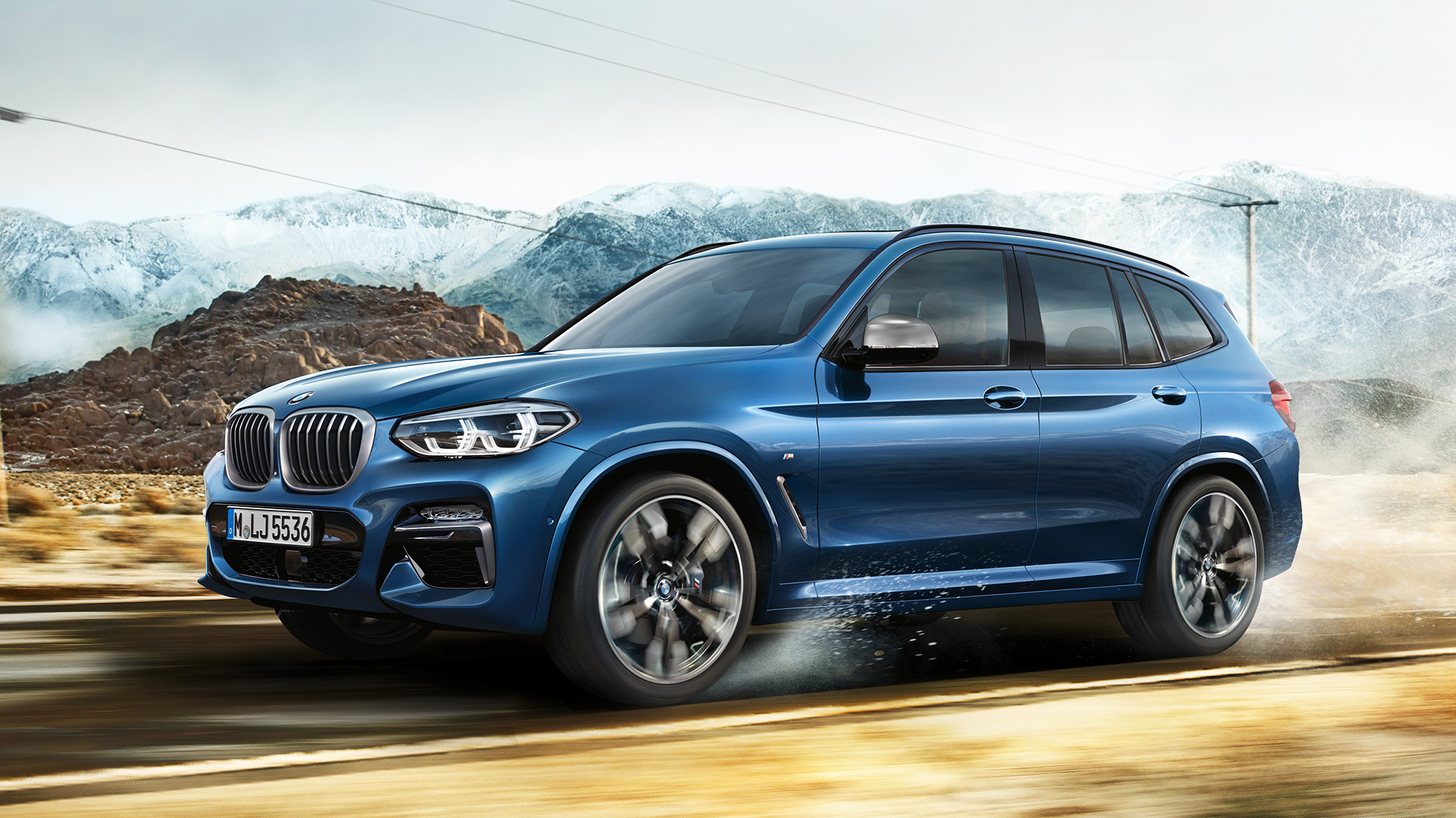 BMW X3 M40i, ratlankio ir priekinio sparno vaizdas iš vidutinio atstumo kalnų fone BMW X3 M40i, ratlankio ir priekinio sparno vaizdas iš vidutinio atstumo kalnų fone