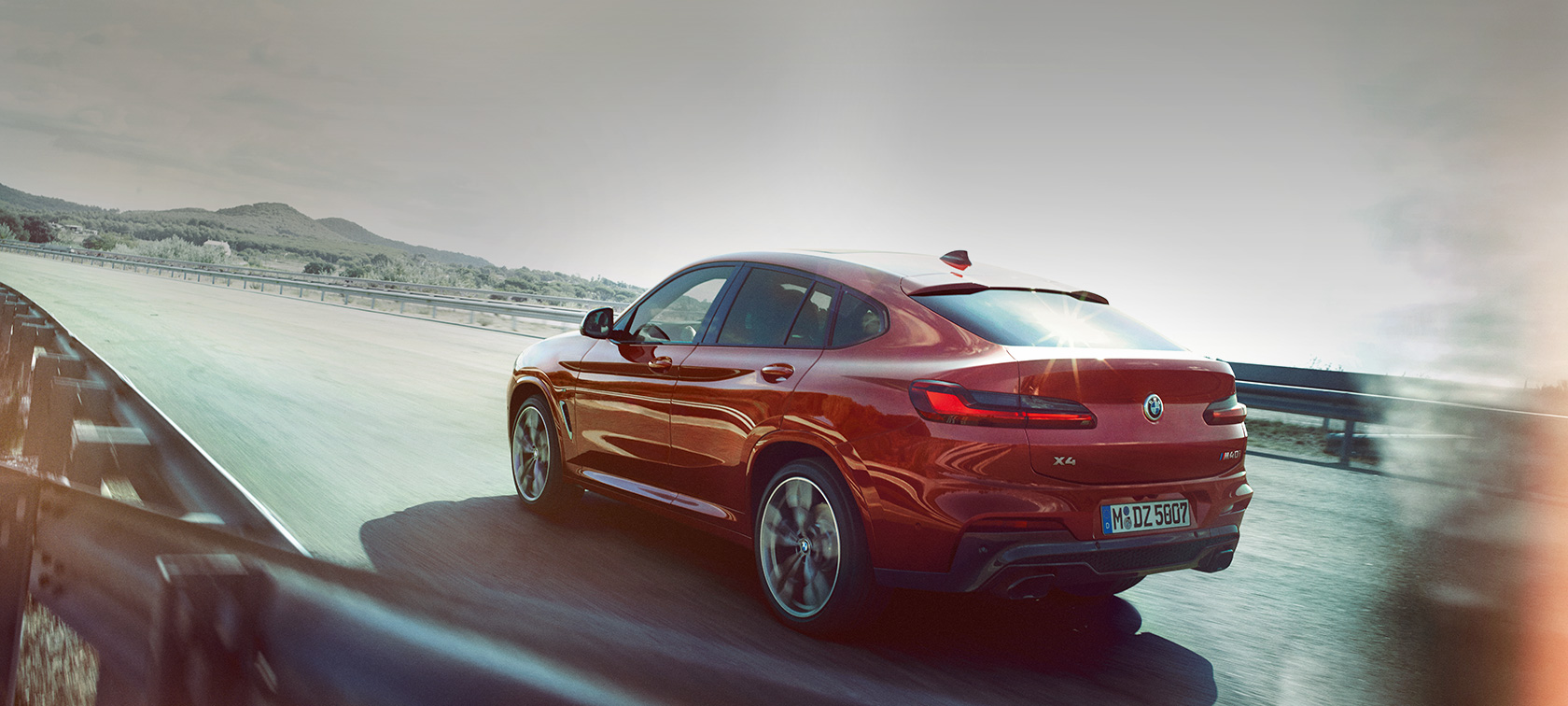 BMW X4 M40i G02 2018 Flamenco Red brilliant effect tviskančios raudonos spalvos keliu važiuojančio automobilio trijų ketvirčių vaizdas iš galo