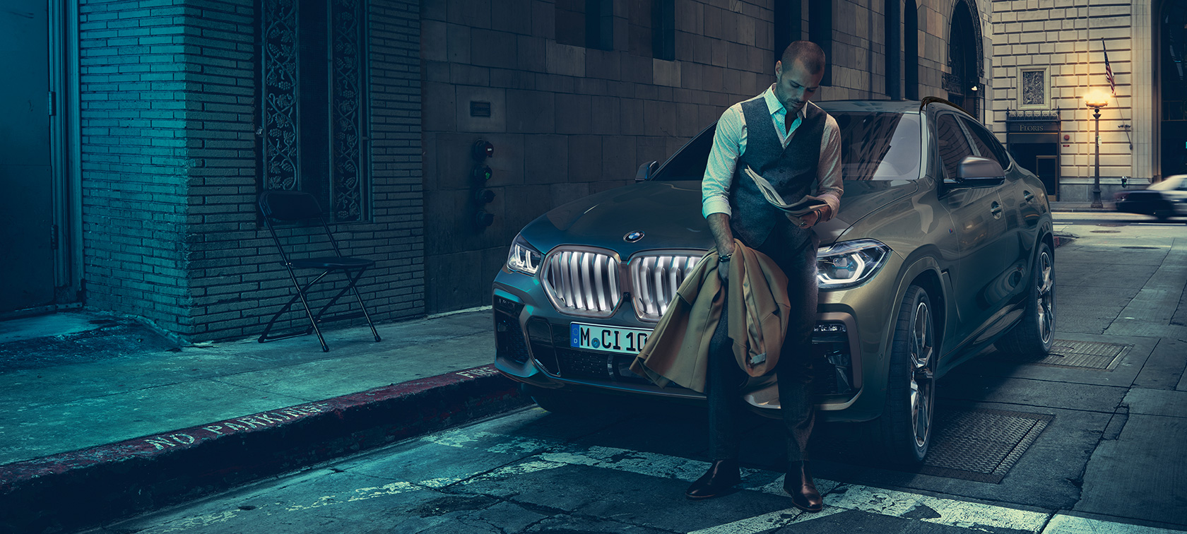 Atsirėmęs į BMW X6 vyras Atsirėmęs į BMW X6 vyras, vaizdas iš šono miesto fone