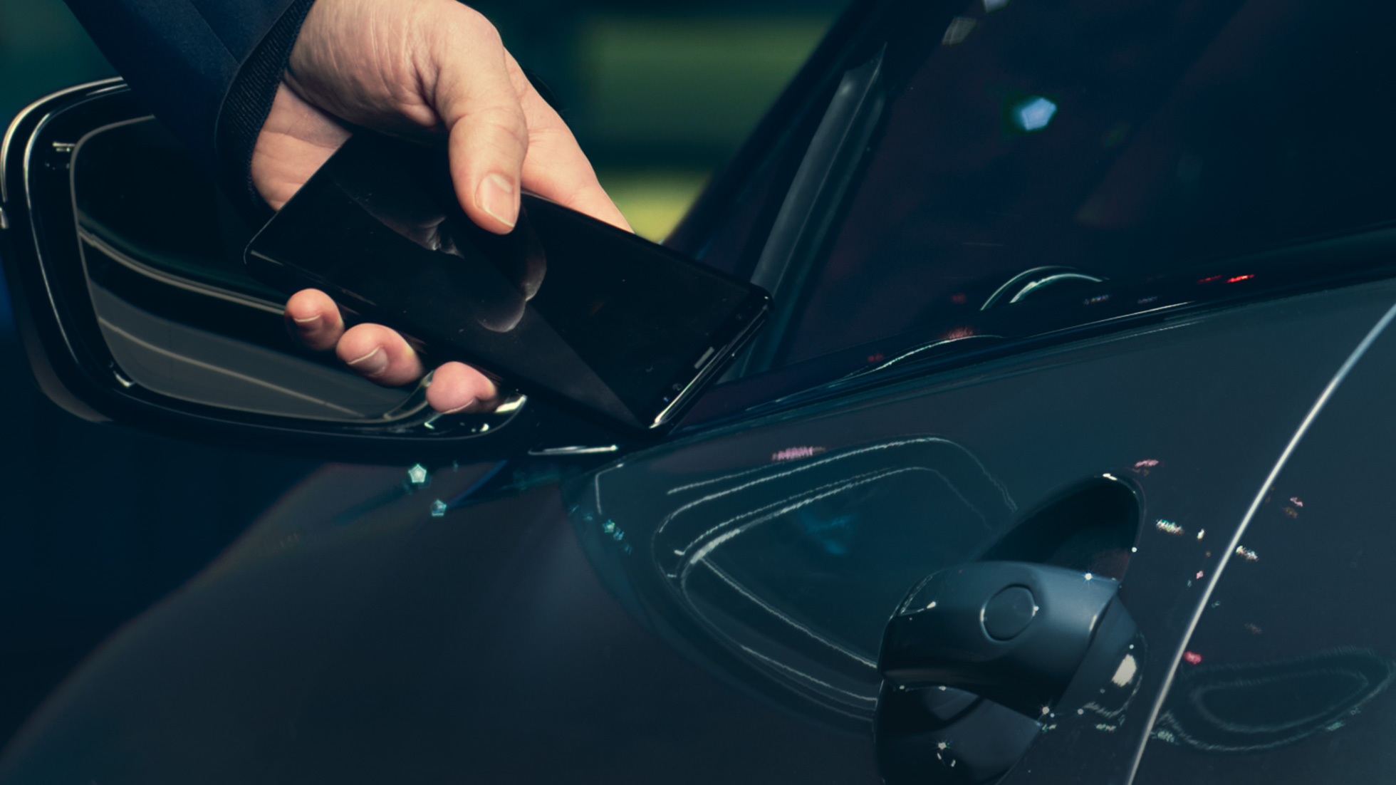 Skaitmeninis raktas Skaitmeninis raktas: Vyras laiko savo išmanųjį telefoną prie automobilio durelių iš išorės
