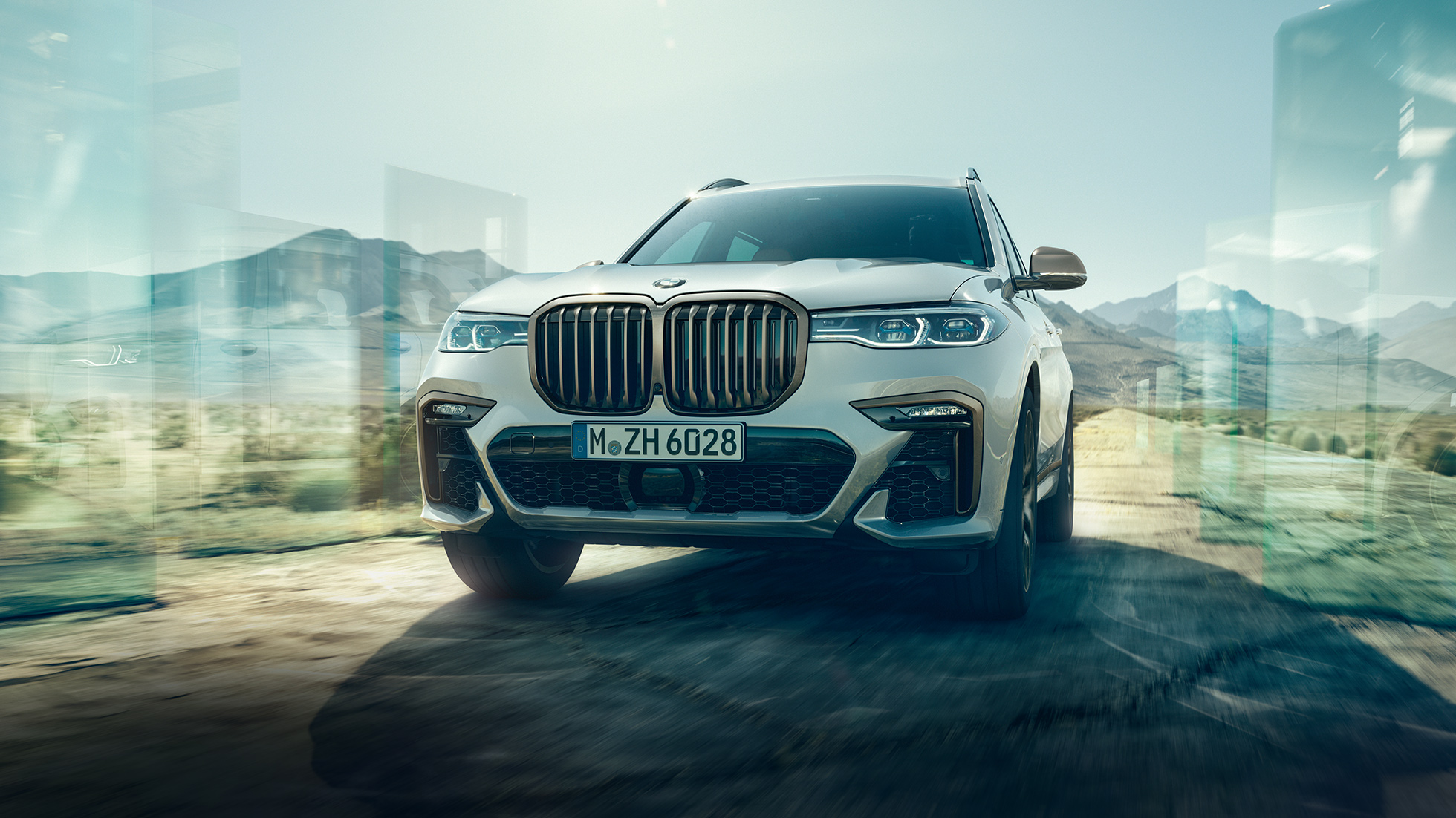 BMW X7 M50d, vaizdas iš apačios BMW X7 M50d: įstrižas važiuojančio balto BMW X7 vaizdas iš apačios