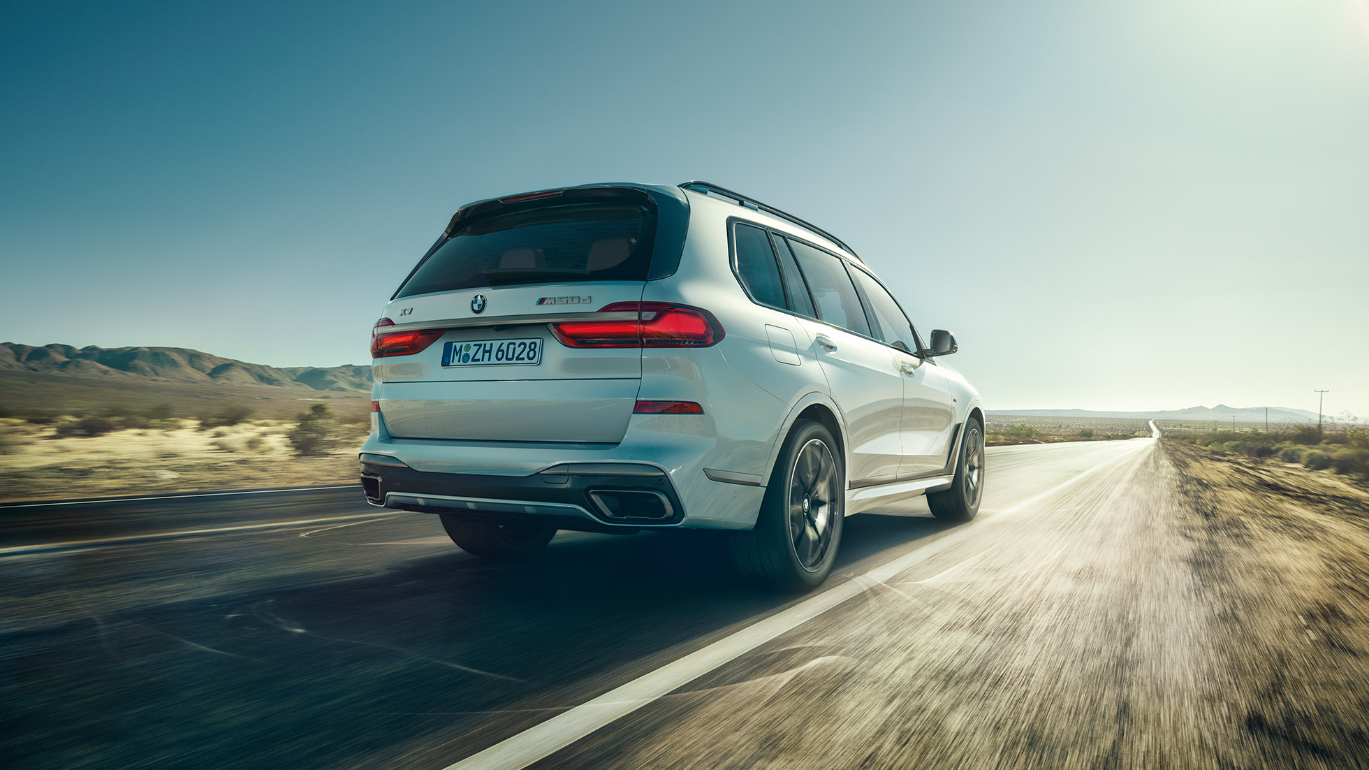 BMW X7 M50d, vaizdas iš galo BMW X7 M50d: važiuojančio balto BMW X7 vaizdas iš galo