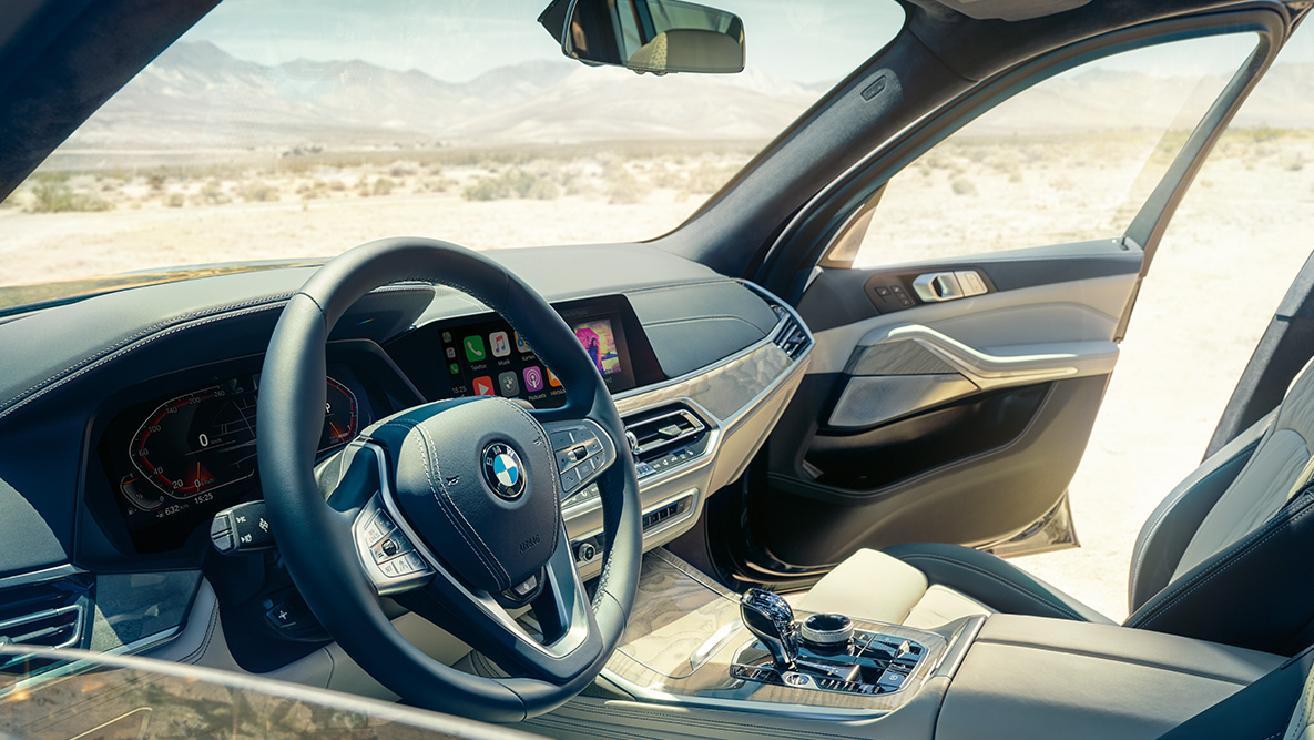 BMW X7 interjeras BMW X7 vidus: vaizdas iš išorės į pirmąją sėdynių eilę, su vairo, prietaisų skydelio ir odinių sėdynių vaizdu