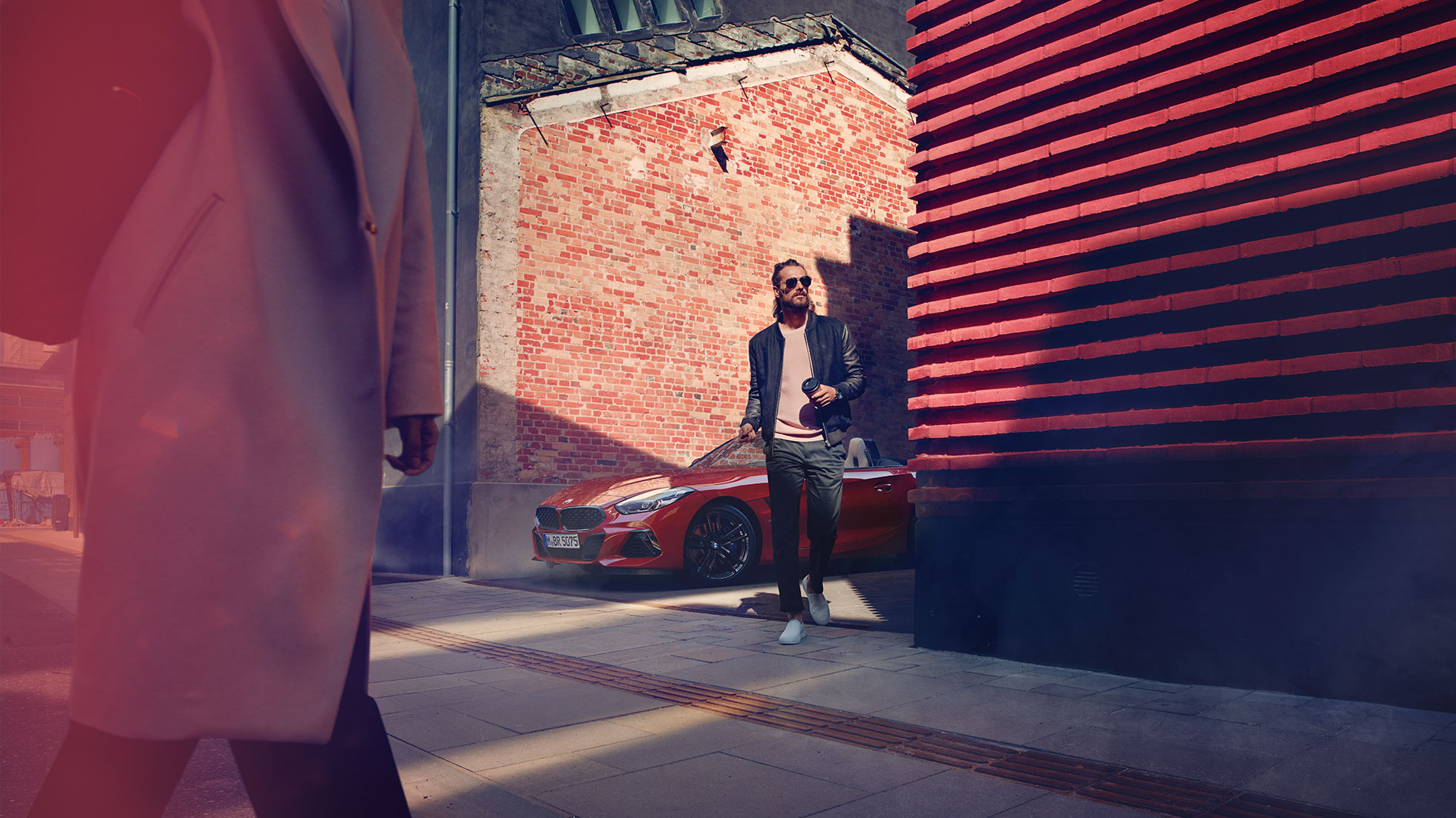 BMW Z4 Roadster siauroje gatvelėje Vyras, stovintis prie BMW Z4 Roadster siauroje gatvelėje