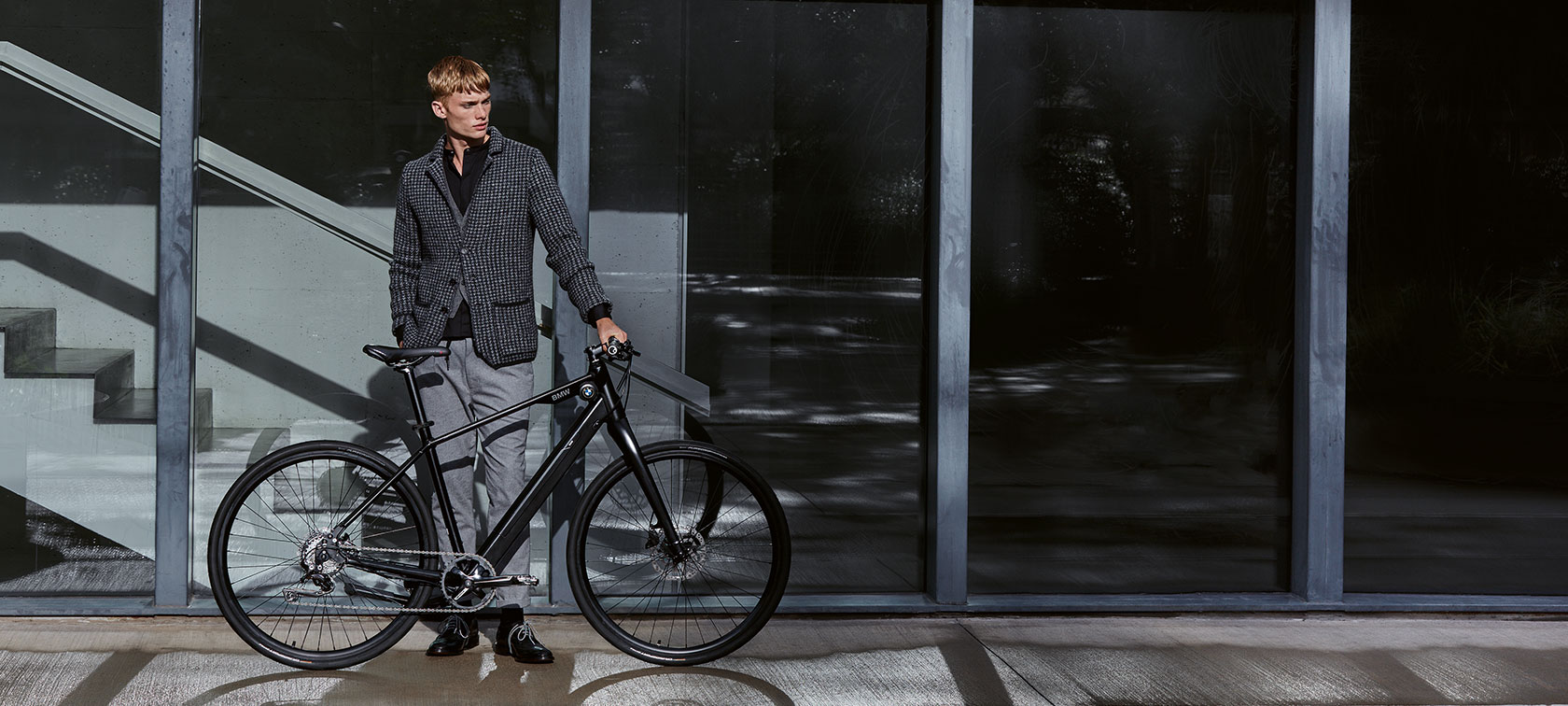 Dizainas ir funkcijos. Vyras nerūpestingai stovi greta „BMW Urban Hybrid E-Bike“ dviračio.