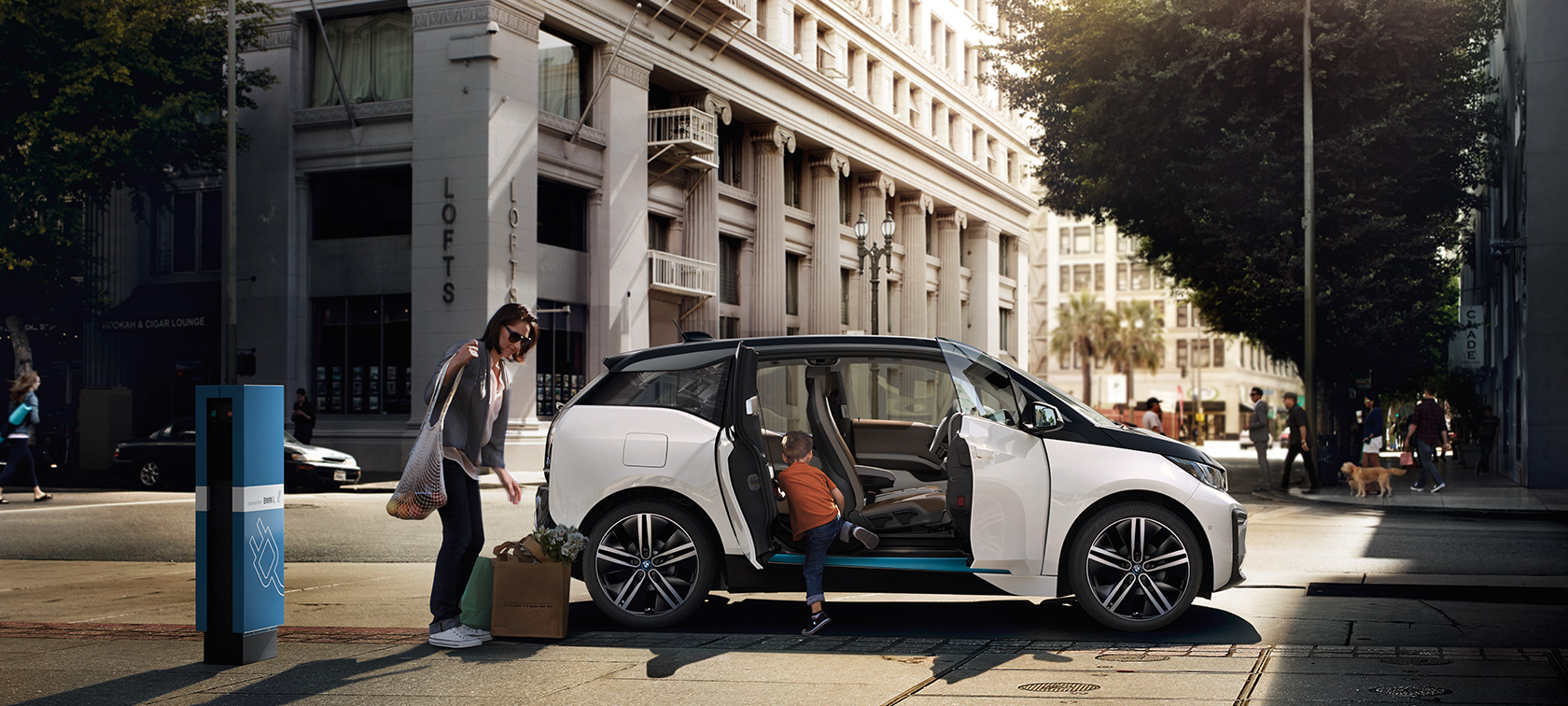 BMW i3s miesto fone BMW nuvažiuojamas atstumas BMW i3 miesto fone su moterimi ir vaiku
