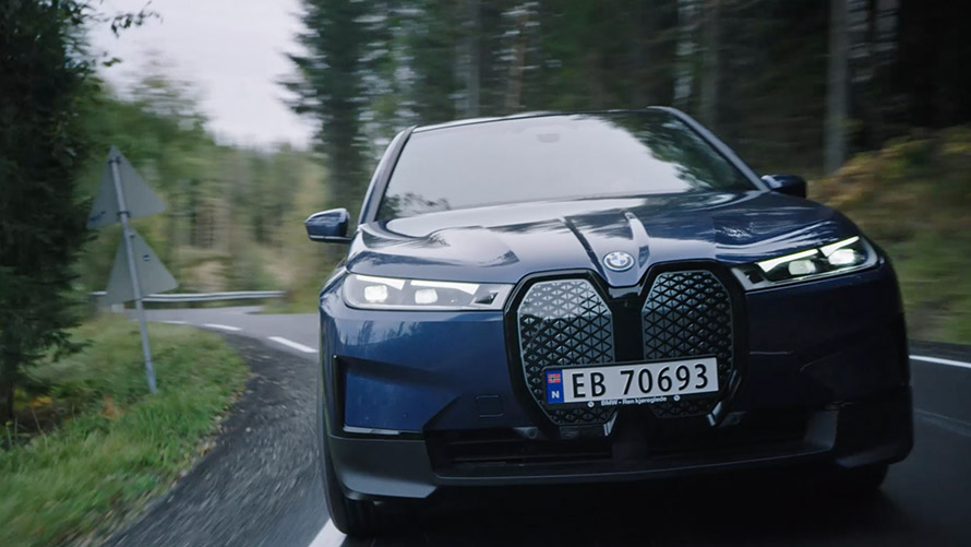 Moteris ruda suknele palinkusi prie BMW iX1 U11 2022 Moteris ruda suknele palinkusi prie BMW iX1 U11 2022 vaizdas iš priekio įkrovimo stotelėje