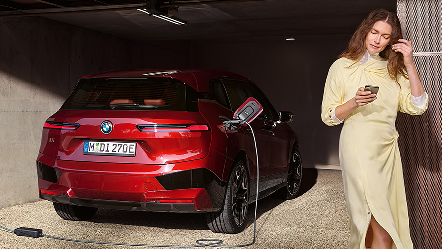 Connected Charging paslauga My BMW programėlėje. Connected Charging BMW App programėlė, šalia įkraunamo BMW i7 xDrive60 stovintis žmogus pirmame plane