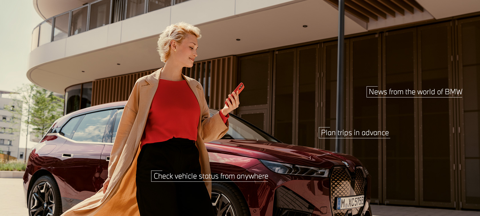 Moteris šalia savo BMW X5 ir naudojasi My BMW programėle savo išmaniajame telefone Moteris šalia savo BMW X5 ir naudojasi My BMW programėle savo išmaniajame telefone