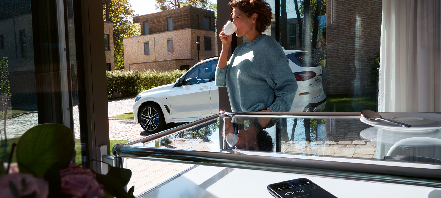 BMW nuotolinis programinės įrangos naujovinimas Moteris, gerianti iš puodelio ir laukianti, kol nuotoliniu būdu bus atnaujinta jos BMW X5 automobilio programinė įranga