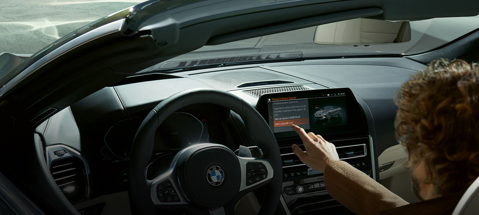 BMW nuotolinis programinės įrangos naujovinimas BMW automobilyje sėdintys vyras, naujovinantis BMW programinę įrangą nuotoliniu būdu.