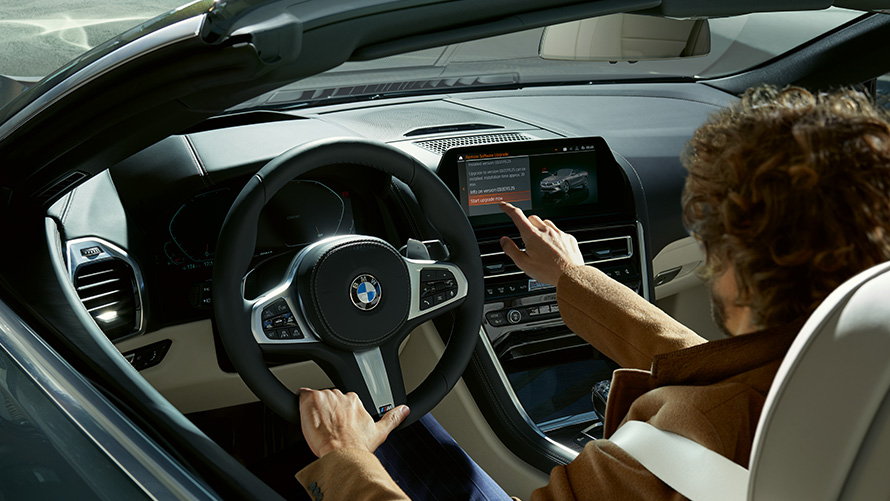 Remote Software Upgrade Nuotolinis programinės įrangos atnaujinimas, vyras sėdi BMW ir naudojasi valdymo ekranu.