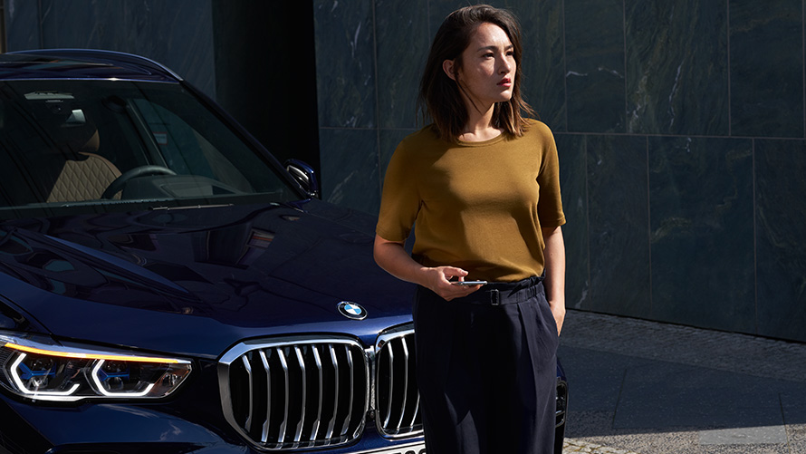 Techninio aptarnavimo ir avarinės pagalbos (Service & Breakdown Assistance) funkcija. Moteris sėdi priešais savo BMW ir naudojasi techninio aptarnavimo ir avarinės pagalbos (Service & Breakdown Assistance) funkcija.