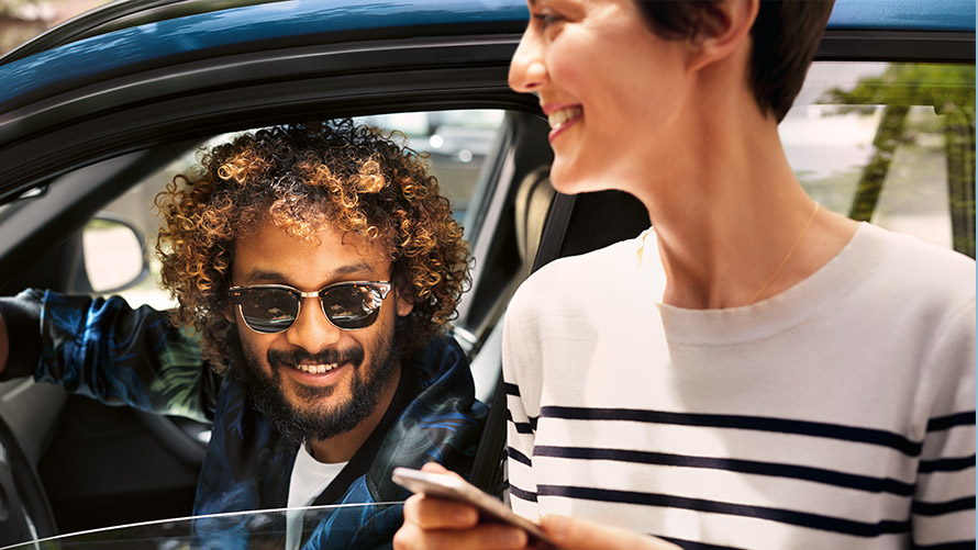 My BMW programėlė Vyras BMW automobilyje ir moteris šalia BMW naudojasi My BMW App programėle savo išmaniuosiuose telefonuose