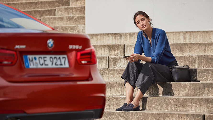 Techninio aptarnavimo ir avarinės pagalbos (Service & Breakdown Assistance) funkcija. Moteris sėdi priešais savo BMW ir naudojasi techninio aptarnavimo ir avarinės pagalbos (Service & Breakdown Assistance) funkcija.