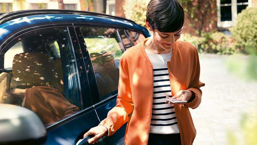 BMW telepaslaugos Moteris su išmaniuoju telefonu rankose stovi prie savojo BMW durelių