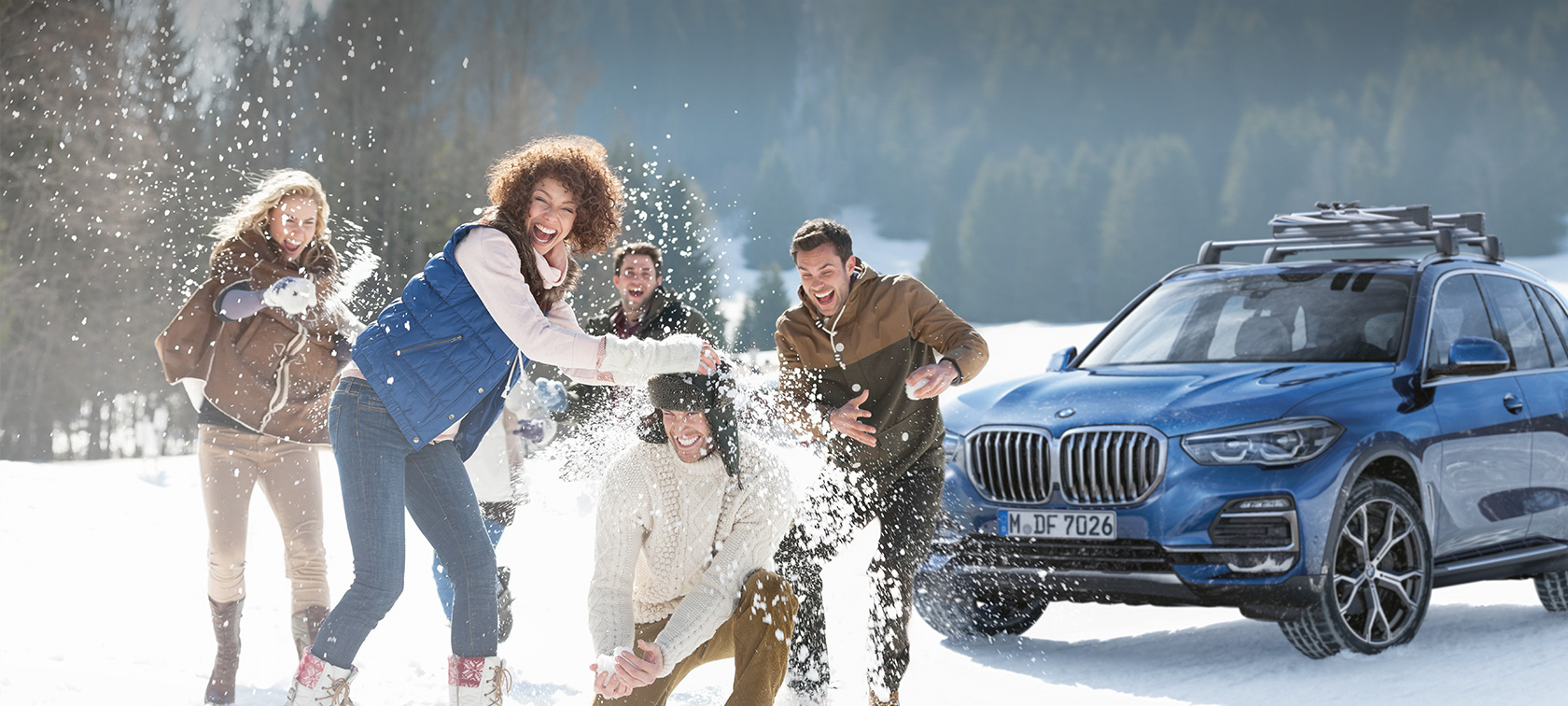 Originalūs BMW aksesuarai ir priedai ir BMW servisas rudens ir žiemos sezonu Besijuokiantys moteris ir vyras, stovintys priešais BMW sniego apsupty