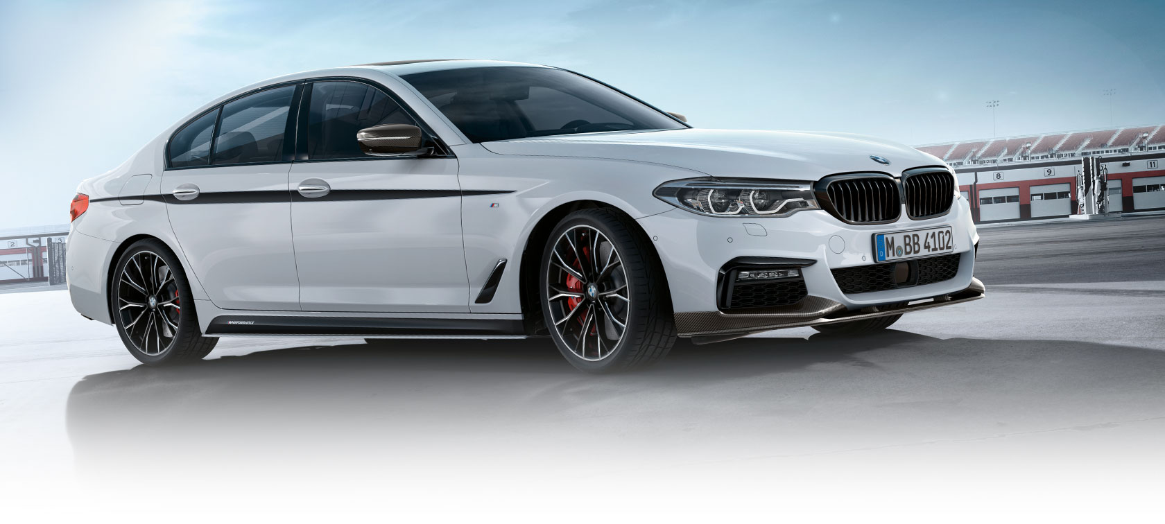 BMW 3 serijos sedanas, „M Performance Parts“ komponentai. BMW 3 serijos sedano šoninis vaizdas automobilių stovėjimo aikštelėje žydro dangaus fone.