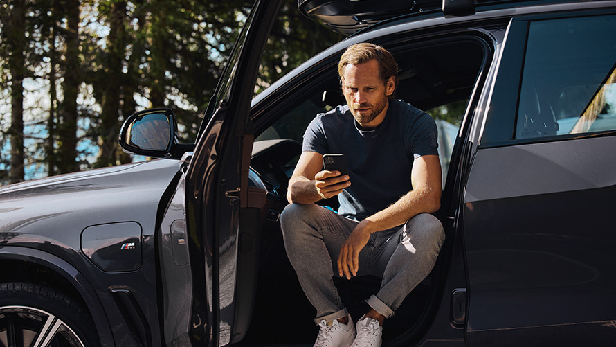 BMW sėdintis vyras su savo išmaniuoju telefonu BMW pavasario vasaros priedai ir aksesuarai, BMW sėdintis vyras su savo išmaniuoju telefonu