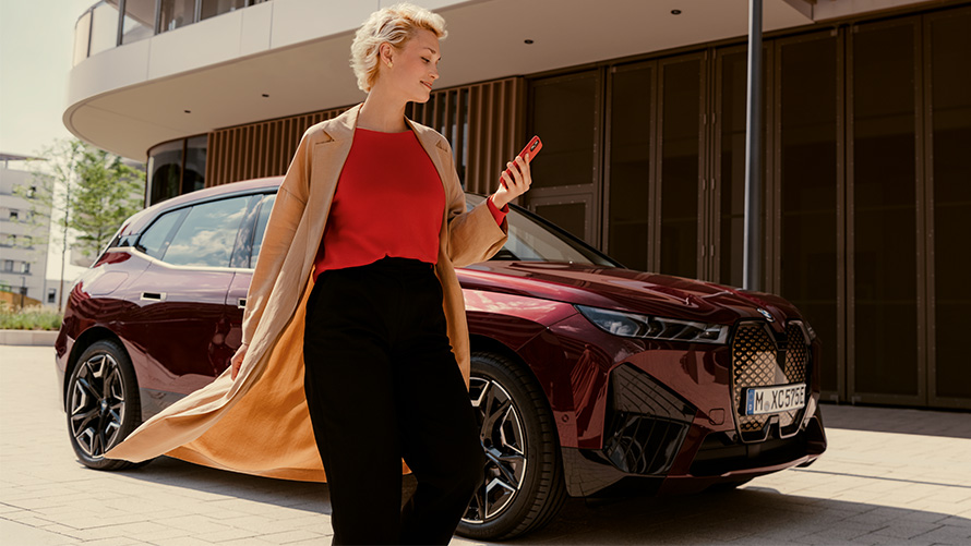 My BMW programėlė, moteris su išmaniuoju telefonu prie BMW automobilio Moteris su išmaniuoju telefonu stovinti priešais BMW