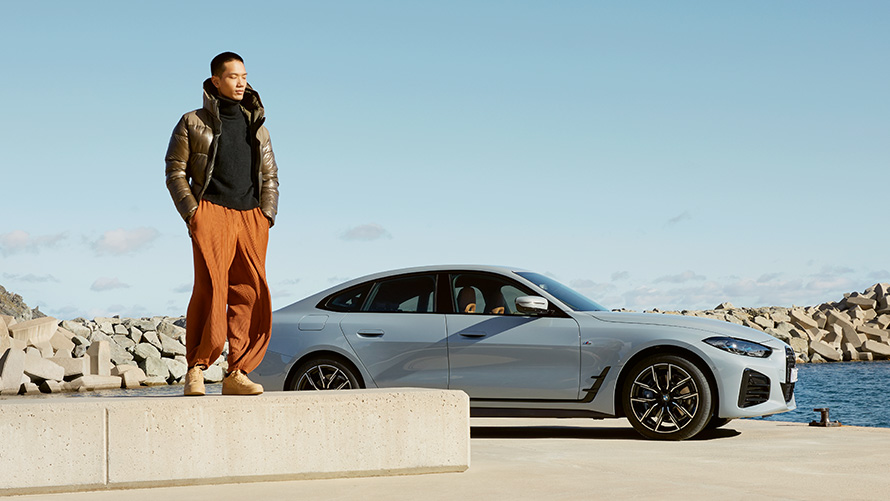 Vasariškame fone stovintis BMW automobilis su pozuojančiu modeliu BMW Service Inclusive paslaugos, vasariškame fone stovintis BMW automobilis su pozuojančiu modeliu