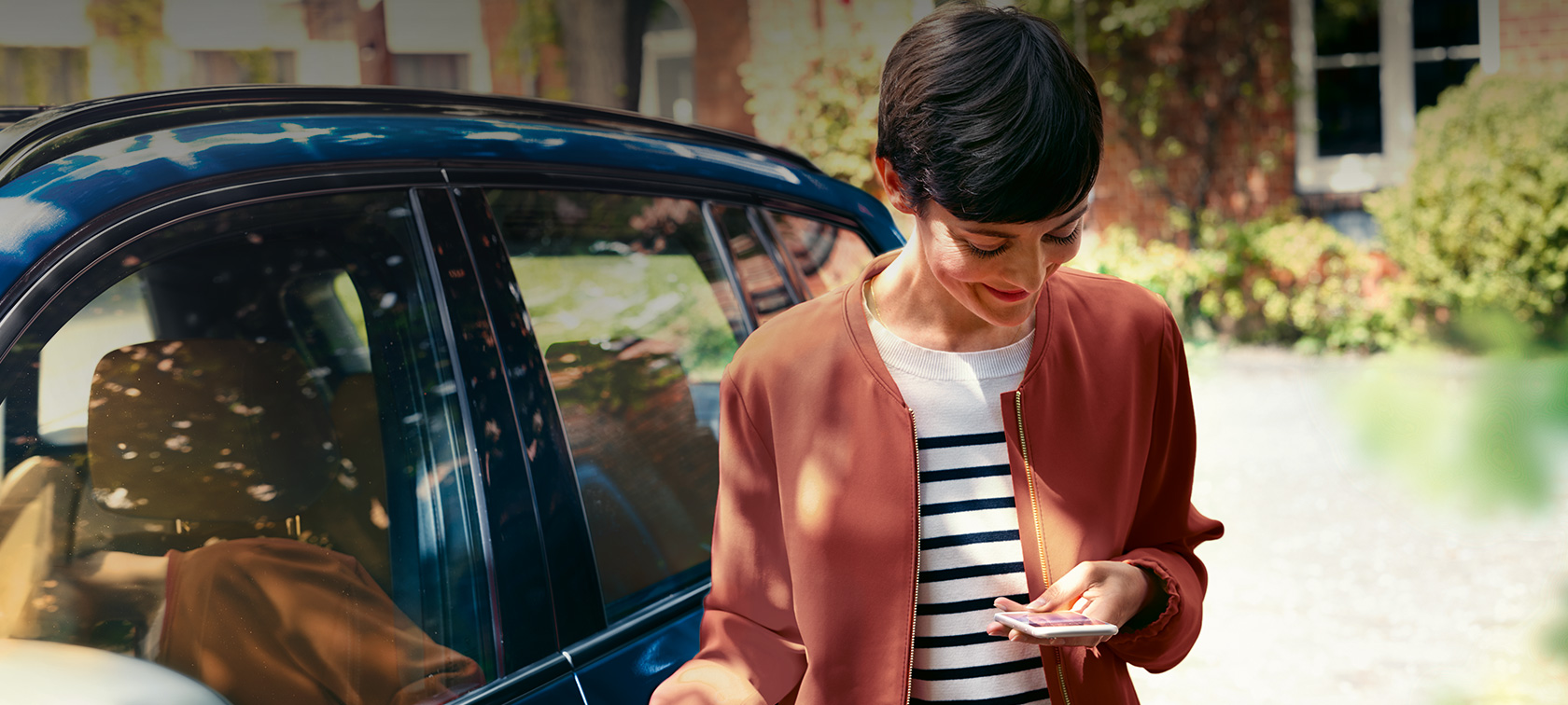 BMW telepaslaugos, savo išmaniuoju telefonu besinaudojanti moteris BMW telepaslaugos, prie BMW automobilio savo išmaniuoju telefonu besinaudojanti moteris