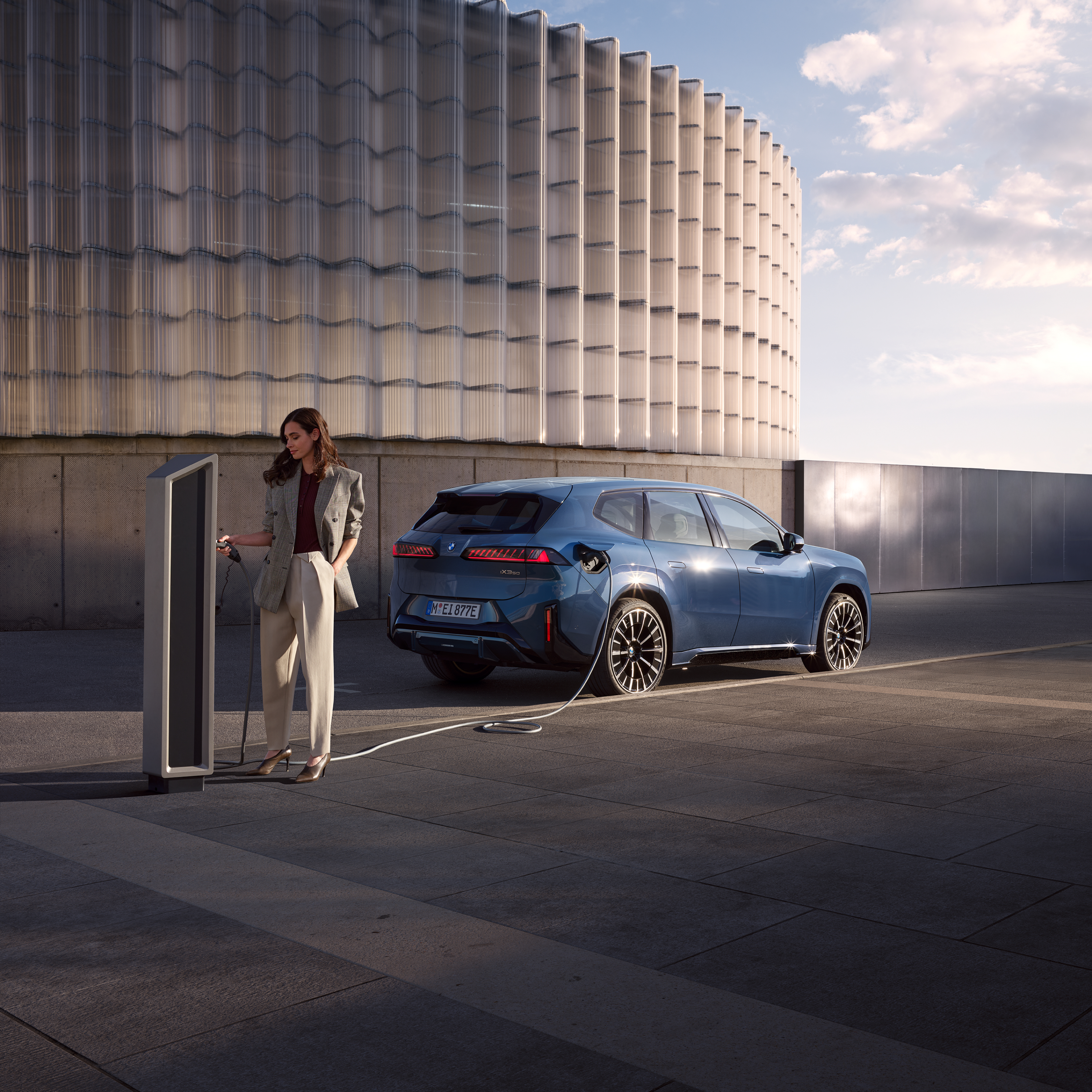 Į viešojo įkrovimo stotelėje įkraunamą BMW iX3 atsirėmęs vyras