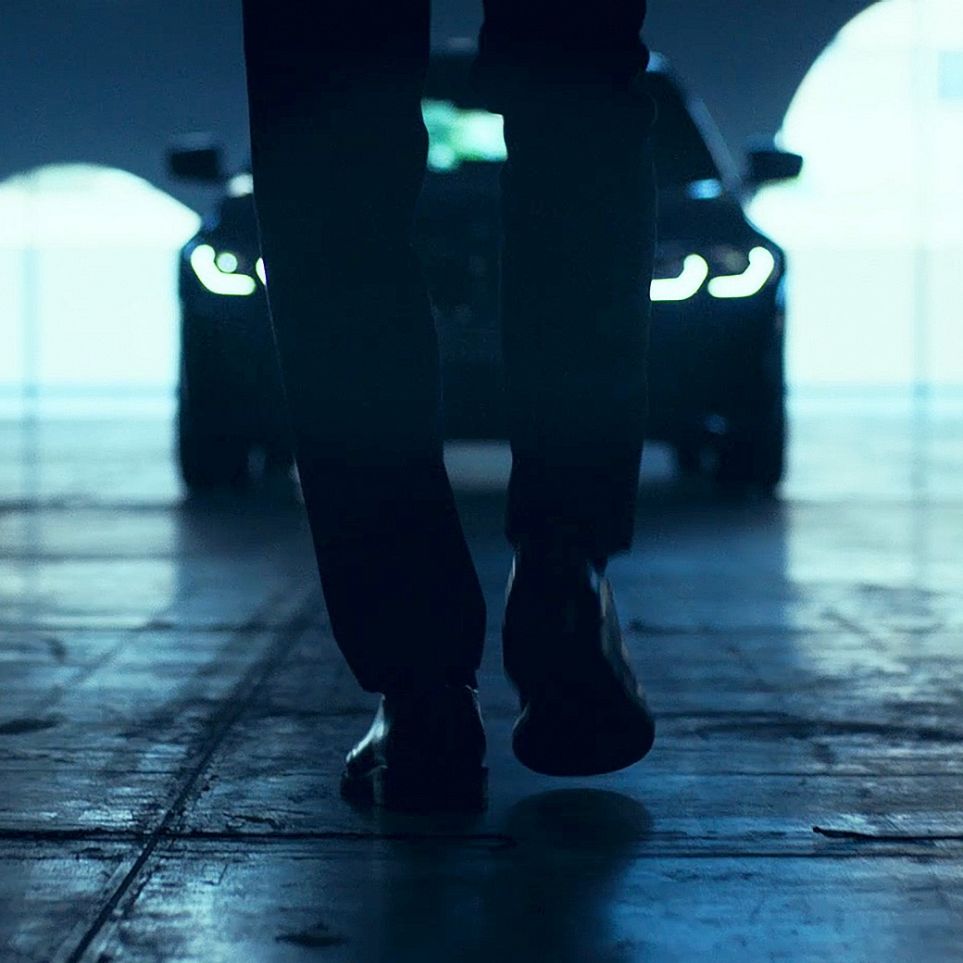 BMW 3 serijos sedanas, priekis Priešais ant asfalto stovintį BMW 3 serijos sedaną praeinantis vyras, vaizdas iš galo